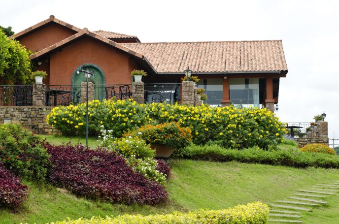 A rustic house surrounded by colorful flower gardens and lush greenery.